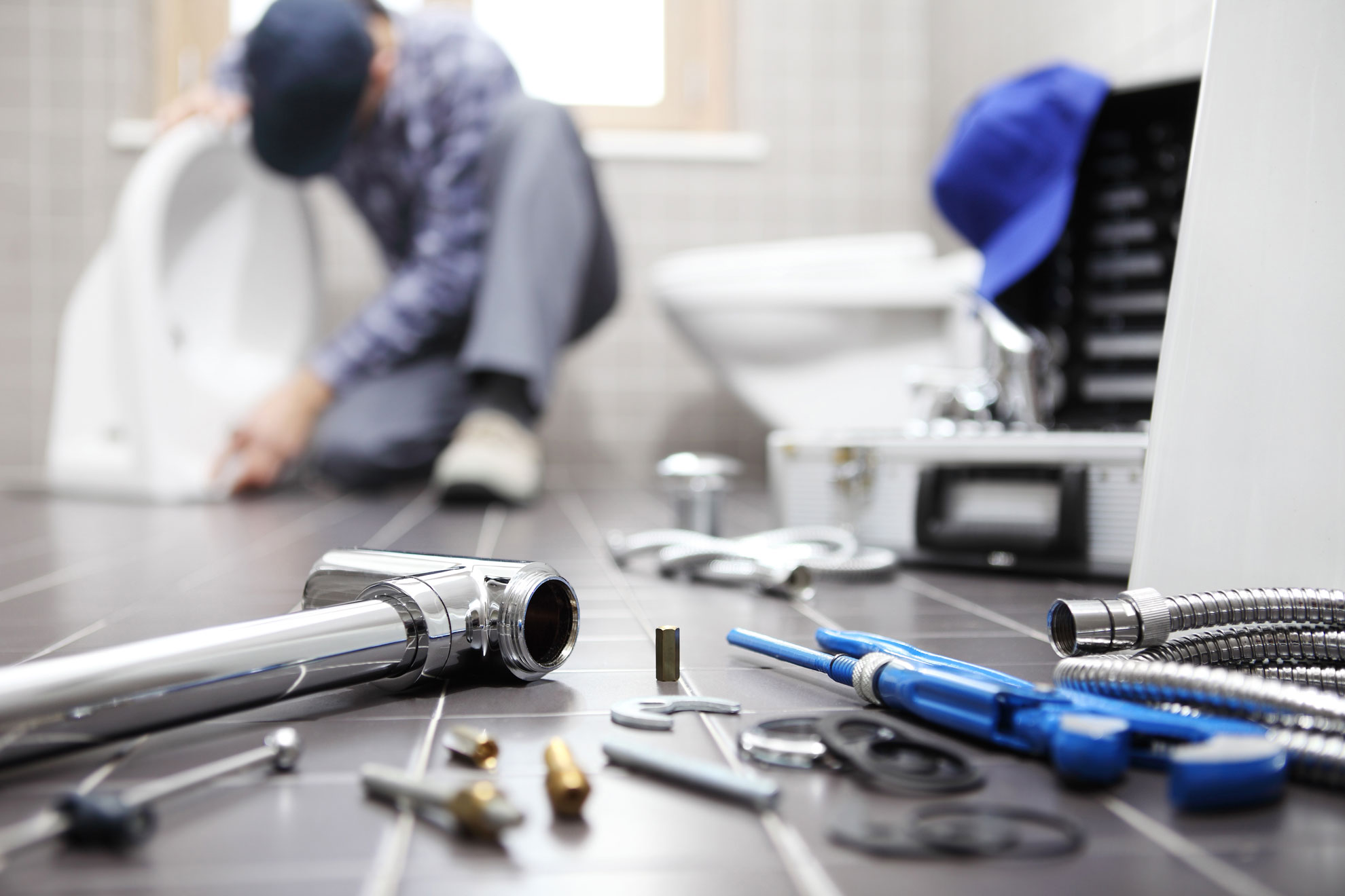 Photo of plumbers tools on floor with plumber in the background fixing a toilet in a home in Holmfirth.